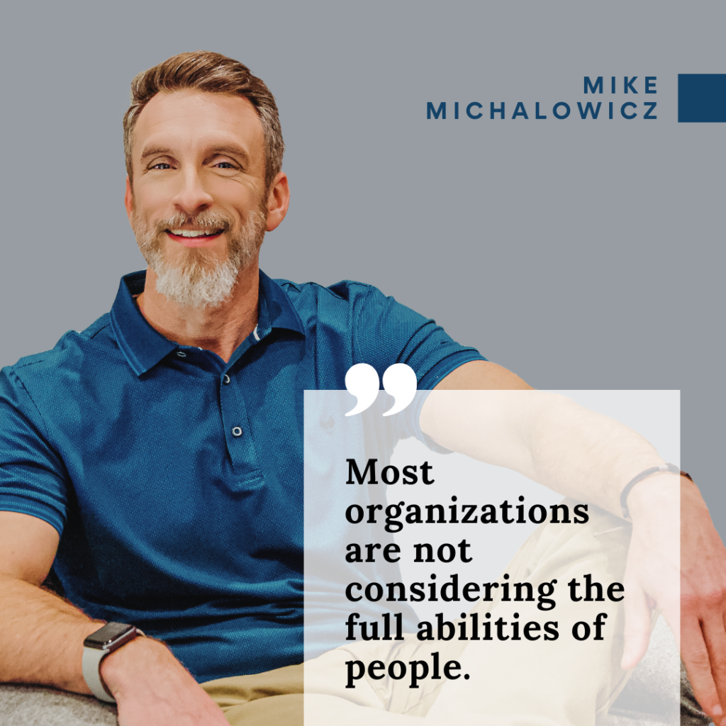 A man with a short beard and mustache, wearing a blue polo shirt, sits and smiles. The text overlay reads, "Most organizations are not considering the full abilities of people." The name "Mike Michalowicz" is in the corner.