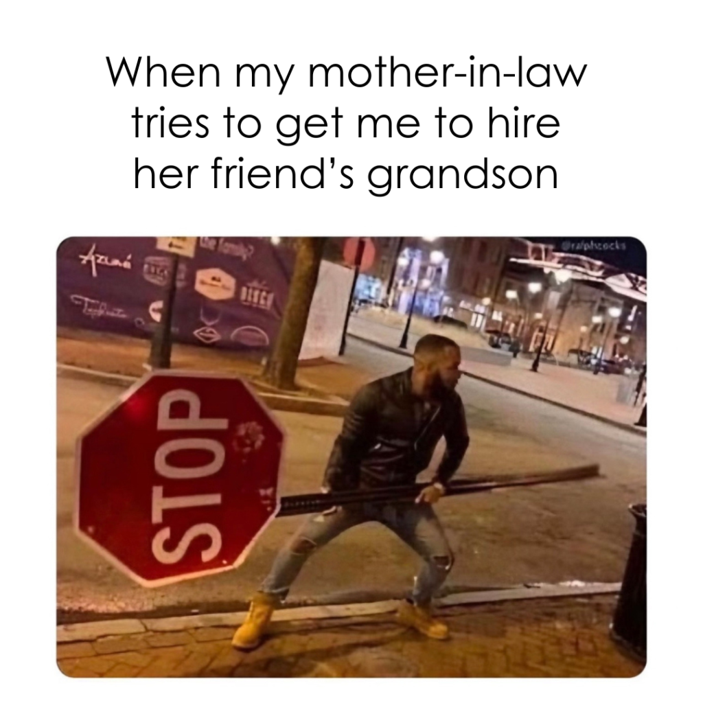 A person standing on a street at night holds a stop sign post like a weapon. The text above reads, "When my mother-in-law tries to get me to hire her friend’s grandson.