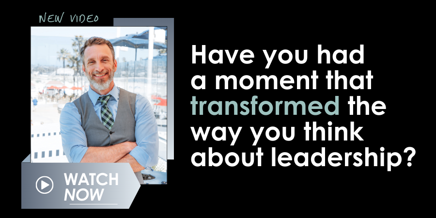 A man in business attire is smiling, standing with his arms crossed. Text reads: "New video. Have you had a moment that transformed the way you think about leadership?" and "Watch Now.
